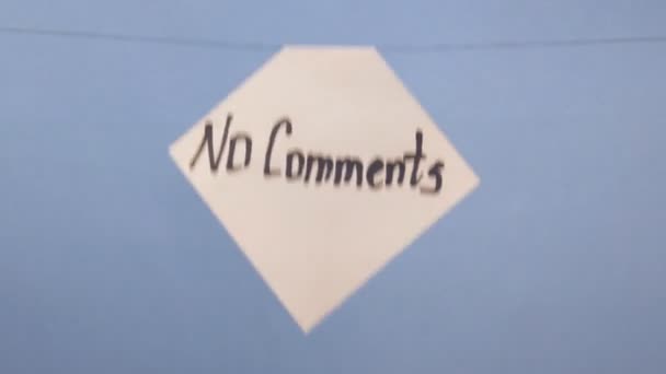 Um homem pendura uma folha branca de papel com uma inscrição preta "sem comentários" em um fundo azul
 - Filmagem, Vídeo
