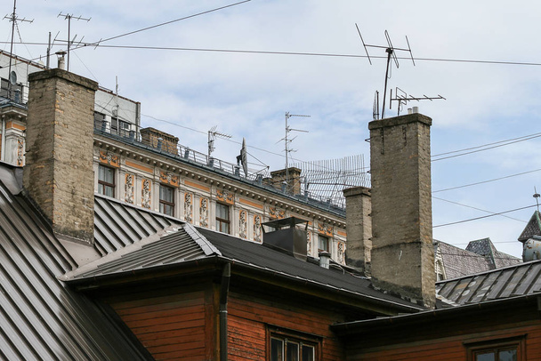 Art Nouveau gebouw naast een oud houten huis met veel tv antennes en schoorstenen op het dak - Foto, afbeelding