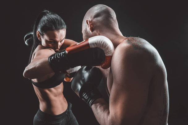 Shirtless Woman exercising with trainer at boxing and self defense lesson, studio, smoke on background. Female and male fight - Foto, immagini