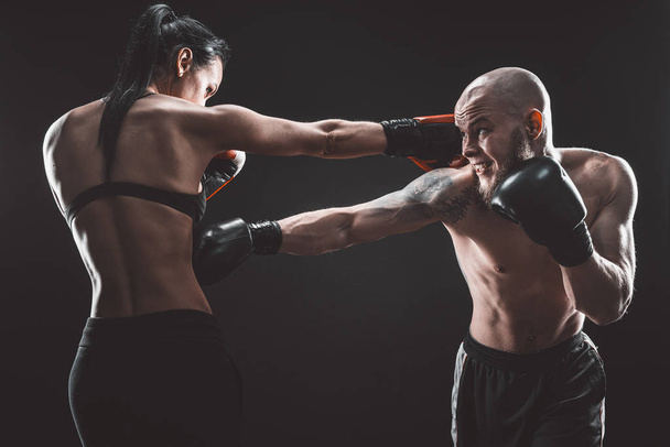 Shirtless Woman exercising with trainer at boxing and self defense lesson, studio, smoke on background. Female and male fight - 写真・画像