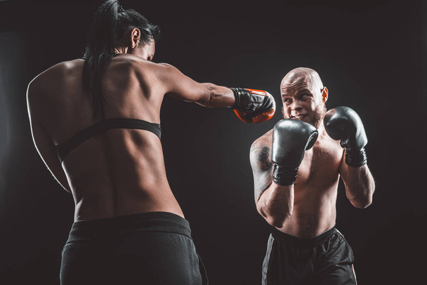 Shirtless Woman exercising with trainer at boxing and self defense lesson, studio, smoke on background. Female and male fight - Fotografie, Obrázek