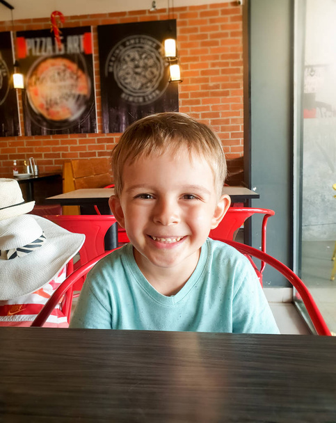 Kafede oturan ve kameraya bakan mutlu çocuk portresi. - Fotoğraf, Görsel
