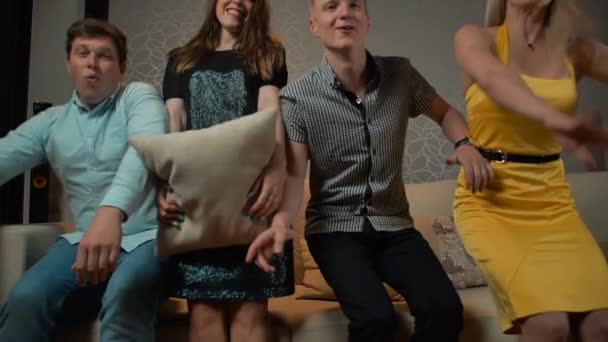 Young people falling down on sofa to watch TV with pillow or cushion - Video