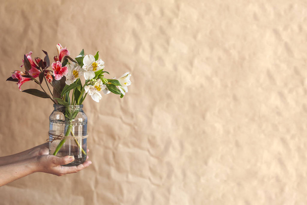 Donna regge un vaso di vetro di bellissimi fiori primaverili colorati
 - Foto, immagini