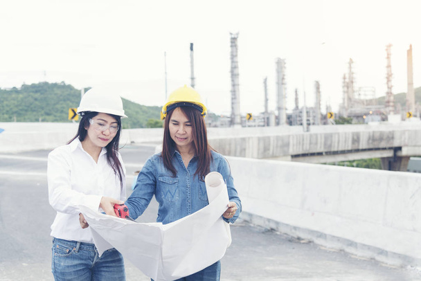 Ingeniera mujer inteligente sosteniendo el sombrero blanco en la mano y mira la planta de la industria de refinería en el área del centro de la fábrica de la industria. Concepto de ingeniería
 - Foto, Imagen