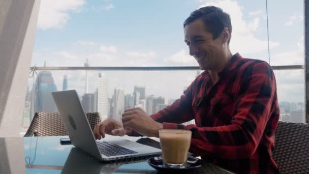 Happy Businessman Sitting Cafe Using Laptop Finishes Project and Wins Big on Background of Big City Skyscrapers. Makes Successful Gestures Raises Arms in Celebration. Gesture yes. - Video