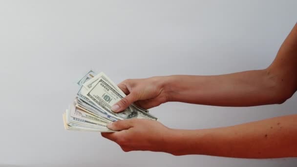 Female hands hold a wad of money and redefine them, close view on white background. Focus on womens hands, in which there are a lot of notes for 100 dollars and 50 euros. Girl recounts cash savings. - Filmmaterial, Video