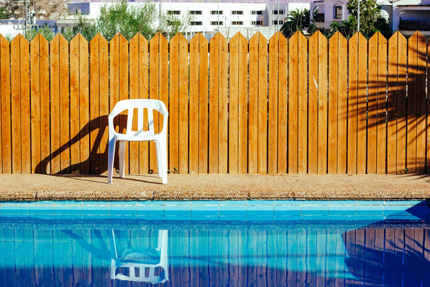 pool side suburban villa back yard space without people here white plastic chair and wooden wall background with lights and shadows in summer sunny day time copy space - Photo, Image