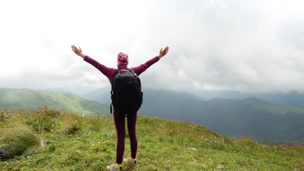 Middle view from the back of a woman tourist who stands near a cliff of a mountain and raises her hands from enjoying the beauty of the landscape from a height in Adygea, Russia. - Felvétel, videó