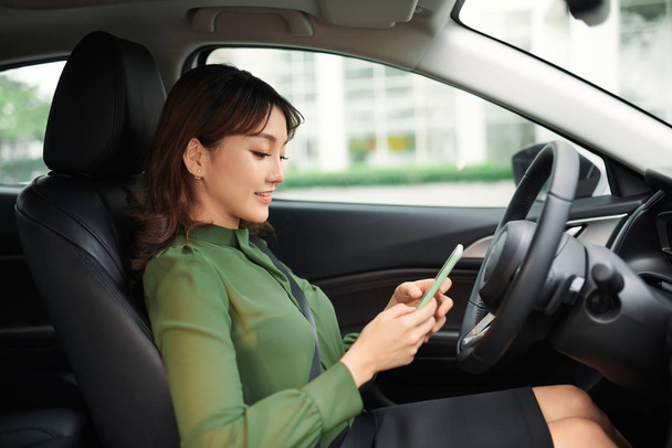Молода жінка за кермом машини дивиться на екран телефону
 - Фото, зображення