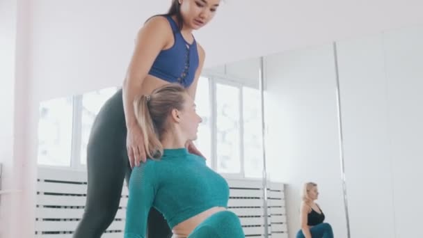Jonge vrouwen doen fitnessoefeningen in de studio - de trainer helpt haar studenten om op de juiste plaats te komen - Video
