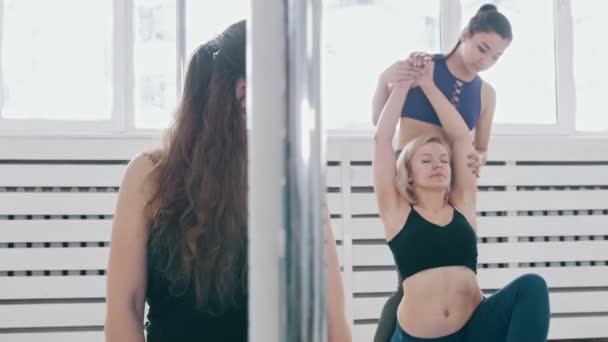 Vrouwen doen fitnessoefeningen in de studio - de trainer helpt haar studenten om in de juiste positie te komen - Video