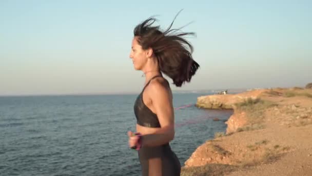 młody dorosły sportowiec dziewczyna szkolenia w pobliżu morza z skakanką - Materiał filmowy, wideo