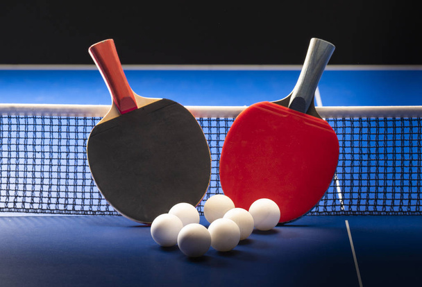 Duas raquetes de tênis de mesa e bolas em uma mesa azul com rede
. - Foto, Imagem