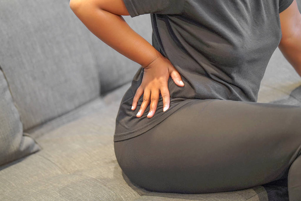 Afrikaans vrouwtje lijdt aan lage rugpijn. De hand van een Afrikaanse vrouw die haar middel pijn doet. Gezondheidszorgconcept. - Foto, afbeelding
