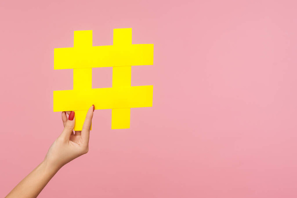 Closeup of hand holding large yellow paper hashtag symbol next to copy space, hash sign of famous media content, social media marketing and blog promotion. studio shot isolated on pink background - Fotó, kép