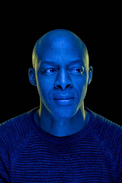 Studioaufnahme mit blauem Licht eines schwarzen Mannes, der zur Seite schaut. Vereinzelt auf schwarzem Hintergrund. Vertikal - Foto, Bild
