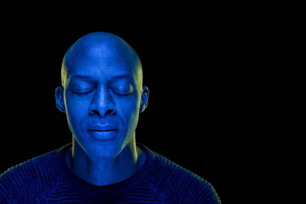 Чорний чоловік з заплющеними очима. Студійна фотографія з синім світлом ізольована на чорному тлі. Концентрація або концепція миру. Горизонтально з копіюванням
 - Фото, зображення