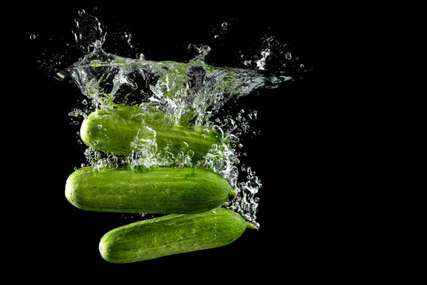 Cucumber splashing water isolated on black background. Skin moisturizing cosmetics - Фото, изображение