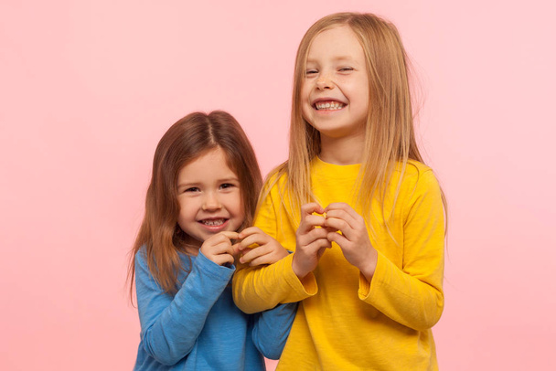 Two funny naughty little girls cunningly looking at camera and plotting tricky plan together, scheming excellent idea to prank friend, bad behavior. indoor studio shot isolated on pink background - 写真・画像