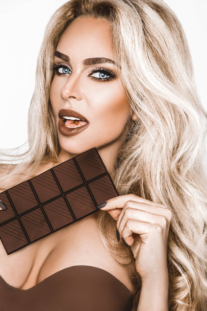 Portrait of a satisfied pretty girl biting chocolate bar and looking at camera isolated over white background. Close-up shot of beautiful woman lips with chocolate, girl licking her lips - Photo, Image