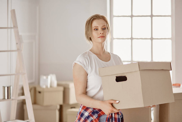 Μια όμορφη ανύπαντρη γυναίκα ξεπακετάρει κουτιά και μετακομίζει σε νέο σπίτι. - Φωτογραφία, εικόνα