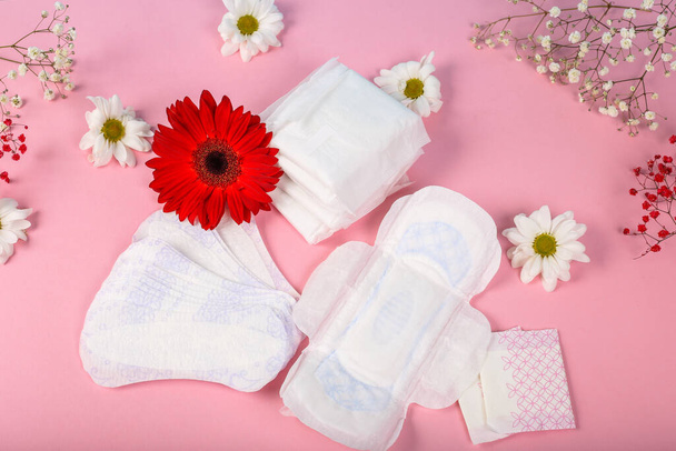 Lot of menstrual pads with red gerbera and white camomile on pink girlish background, top view, copy space. Ovulation concept. menstruation concept. - Фото, изображение