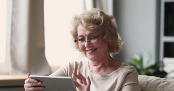 Smiling senior lady wear optical glasses using tablet at home - Felvétel, videó