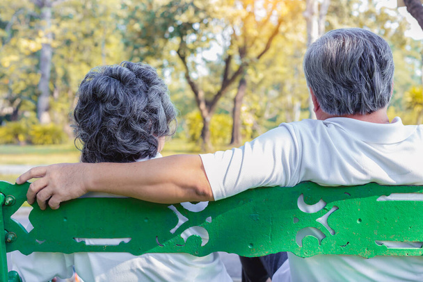 Starsza para lub starsza para azjatycka siedząca na ławce z plecami objętymi w jesiennym parku. Urocza para seniorów rozmawia o swoim życiu i patrzy na piękny widok ze szczęściem. Stara koncepcja pary - Zdjęcie, obraz