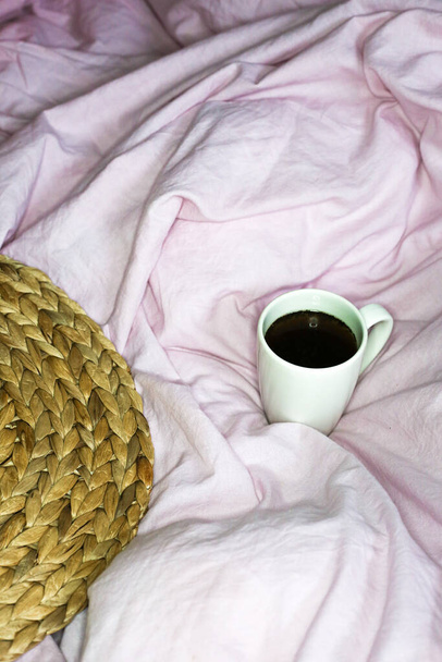 ピンクのベッドシートの背景にモーニングコーヒーマグカップ。綿織物が手を振った.  - 写真・画像
