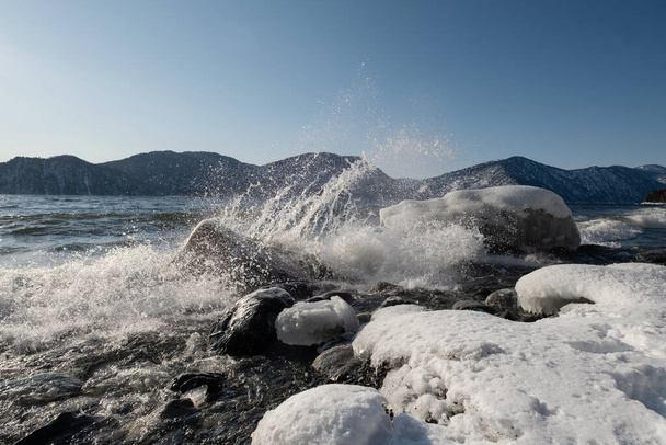Splashing waves in ice water. Winter mountain lake landscape - 写真・画像