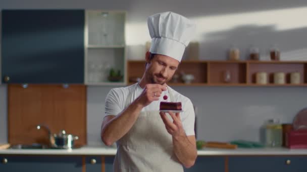 Baker putting cherry on cake at workplace. Chef man smiling at camera on kitchen - Video