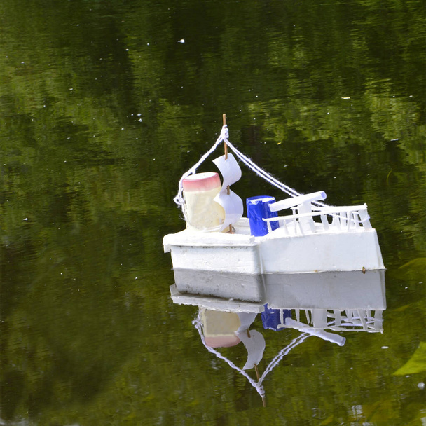 Auf dem Fluss schwimmt ein selbst gebasteltes Kriegsschiff für Kinder. Boot mit Segel spiegelt sich im Wasser, aus nächster Nähe. Ein Schiff mit Gewehr schwimmt auf einem Teich. Der Blick von der Seite. - Foto, Bild
