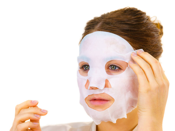 Woman applying sheet mask on her face, on white. Girl taking care of skin complexion. Beauty treatment. Skincare. - Photo, Image
