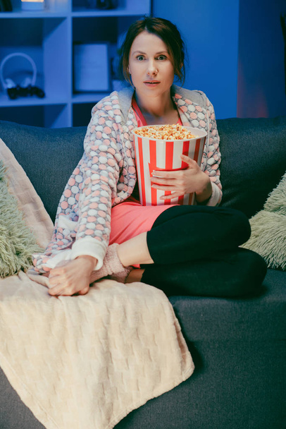 Happy beautiful girl face watching comedy film in home. Millennial woman sitting on sofa and watching TV. Concept of entertainment. Positive emotions. - 写真・画像