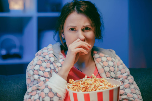 Young woman cry while watching a very moving movie with popcorn at night - Fotoğraf, Görsel
