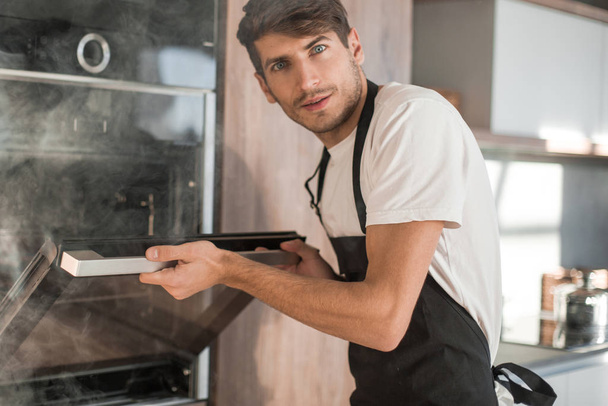 frustrated young man standing near broken oven - Foto, Imagen