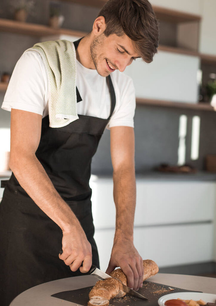 молодий чоловік готує бутерброд на кухні
 - Фото, зображення
