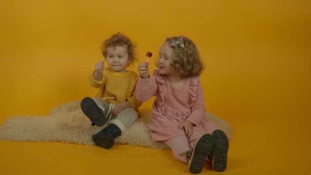 Two curly smiling kids sitting on carpet with lollipops - Footage, Video