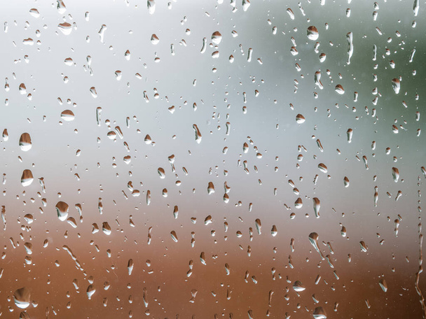 雨は曇った背景の窓ガラス表面に落ちる。ぼやけた背景に隔離された雨滴の自然なパターン. - 写真・画像