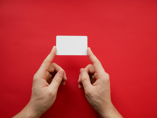 Mãos femininas segurando cartão branco branco branco no fundo vermelho. Vista superior
 - Foto, Imagem