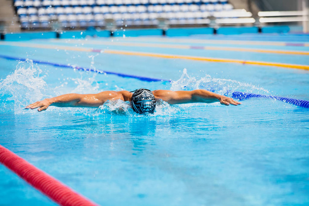 Athletic man swimming in butterfly style in the swimming pool with clear blue water. - 写真・画像