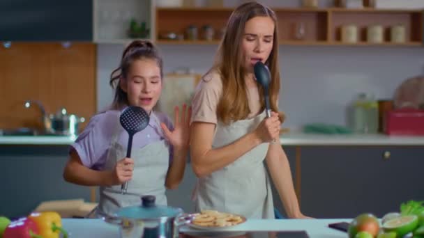 Iloinen äiti ja tytär laulavat laulun lusikoissa keittiössä
 - Materiaali, video