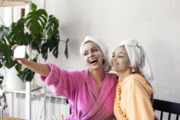 Mother and her daughter taking selfie by phone with facial mask and towel on head - Photo, Image