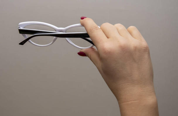 Το γυναικείο χέρι κρατά γυαλιά, επιλογή γυαλιών για βελτίωση της όρασης σε γκρίζο φόντο, συστάσεις οφθαλμιάτρων και οπτομετρικών, οπτικών και πλαισίων. - Φωτογραφία, εικόνα