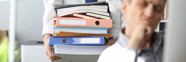 Homme portant une grosse pile de documents à un collègue malheureux
 - Photo, image