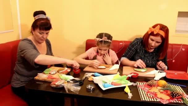 女の子がテーブルでジンジャーブレッドクッキーを飾る若い女性 - 映像、動画