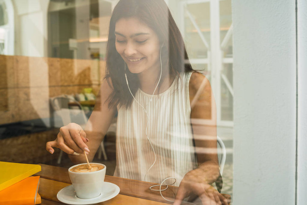 Portret van een jonge Latijnse vrouw die geniet en een kop koffie drinkt in de coffeeshop. Levensstijl concept. - Foto, afbeelding