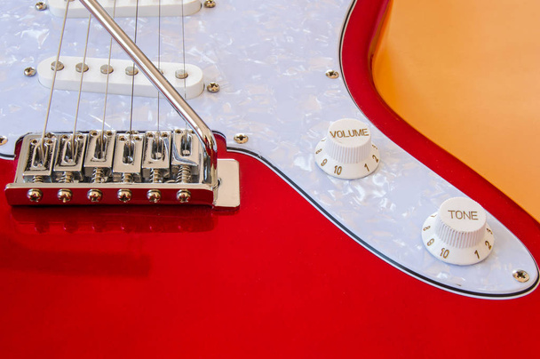 Parte de una guitarra eléctrica roja y blanca sobre fondo naranja. Vistas de la barra de vibrato y botones de volumen y tono
. - Foto, imagen