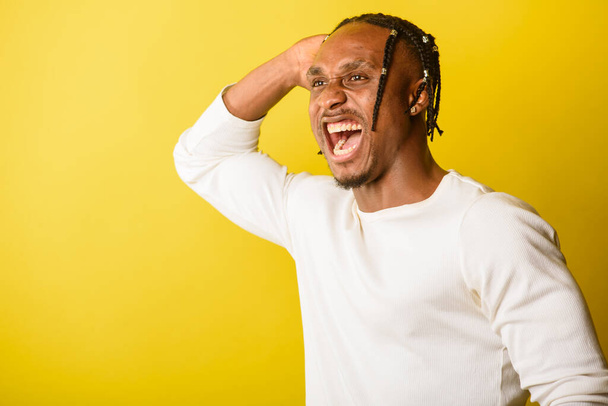 retrato de un joven negro, aspecto africano, emocional y serio y mirando hacia arriba, agitando sus manos, de rastas, sobre fondo amarillo
  - Foto, Imagen